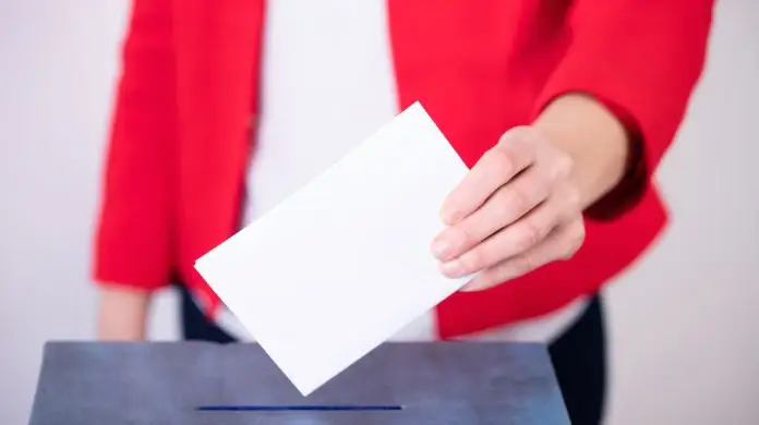 Obietnice wyborcze dla rynku pracy - wybory - kobieta trzymająca kartę wyborczą nad urną