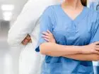 Pielęgniarka stojąca w korytarzu na tle innych pracowników medycznych