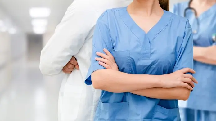 Pielęgniarka stojąca w korytarzu na tle innych pracowników medycznych