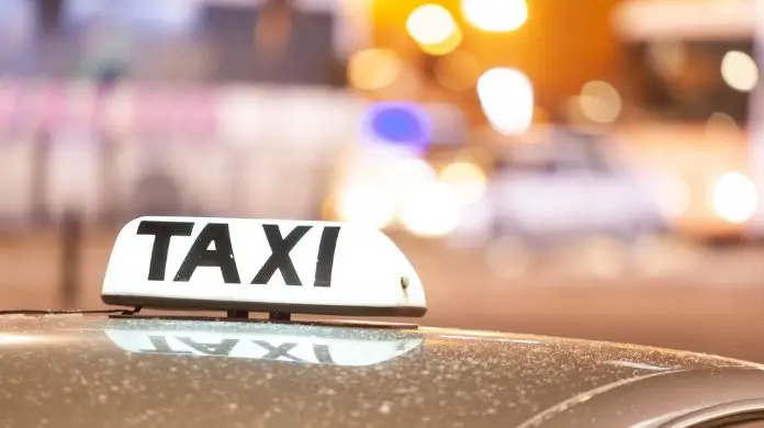 Protest taksówkarzy - świecący napis taksówki z bliska na tle przejeżdżających samochodów na nocnej ulicy dużego miasta