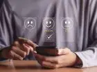 Ocena pracownika - telefon w dłoni człowieka, nad telefonem trzy twarze wyrażające różne emocje z ocenami pod spodem