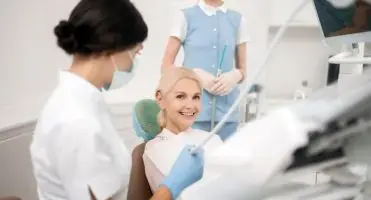 Szczęśliwa kobieta w klinice dentystycznej siedzi w gabinecie dentystycznym i uśmiecha się, czekając na rozpoczęcie leczenia stomatologicznego