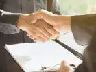 Zdjęcie przedstawiające dwie osoby podające sobie dłoń nad dokumentem umowy