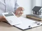 Wakacje kredytowe 2024 - próg dochodowy - symboliczne zdjęcie przedstawiające kobietę dokonującą obliczeń na kalkulatorze na tle dokumentów