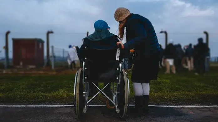 9460 świadczenia wspierającego - symbolcizne zdjęcie rpzedstawiające opiekuna z osobą z niepełnosprawnością na wózku