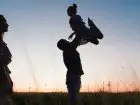 opieka naprzemienna - ojciec trzymający dziecko na rękach na polu, matka przygląda się z boku