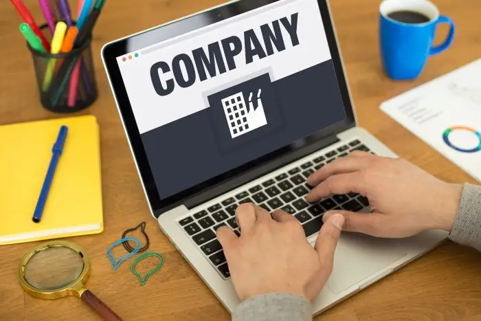 Laptop z napisem company na ekranie, wokół na blacie przybory biurowe