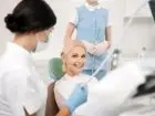 Szczęśliwa kobieta w klinice dentystycznej siedzi w gabinecie dentystycznym i uśmiecha się, czekając na rozpoczęcie leczenia stomatologicznego