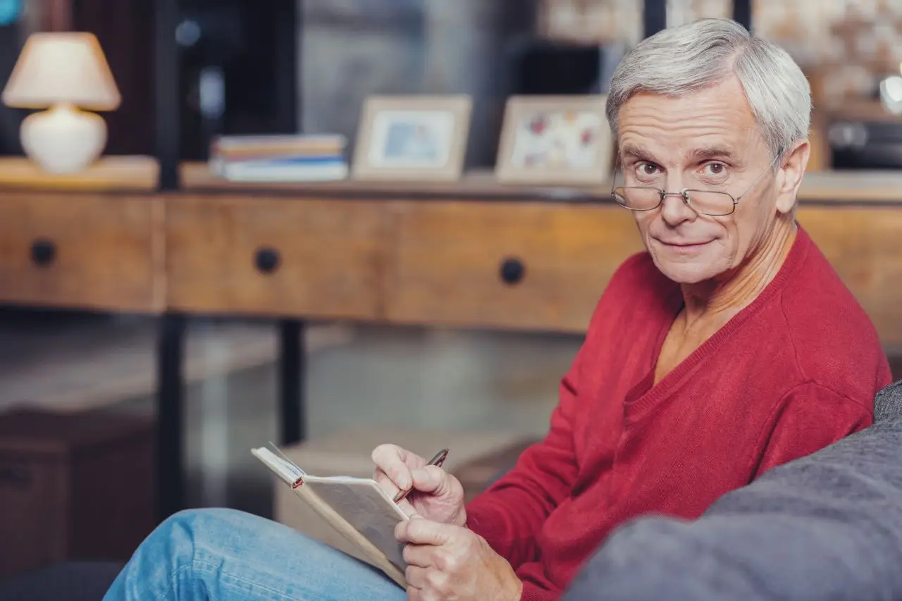 Ile można dorobić do renty 2024 - mężczyzna siedzący na kanapie, w okularach, używa notesu