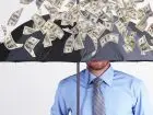 Ekwiwalent Przyłębska - symboliczne zdjęcie przedstawiające mężczyznę, który stoi z parasolem chroniąc się przed deszczem pieniędzy