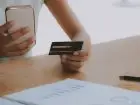Ile idzie przelew - kobieta trzymająca w dłoni kartę płatniczą, a w drugiej telefon