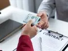 Kaucja - zbliżenia na dłonie osoby, która wręcza drugiej kaucję nad umową