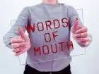 Przeklinanie w pracy - osoba trzymająca w dłoniach pleksi z napisem "words of mouth"