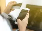 Przelew kontrola - telefon w jednej dłoni kobiety, w drugiej karta płatnicza, w tle laptop