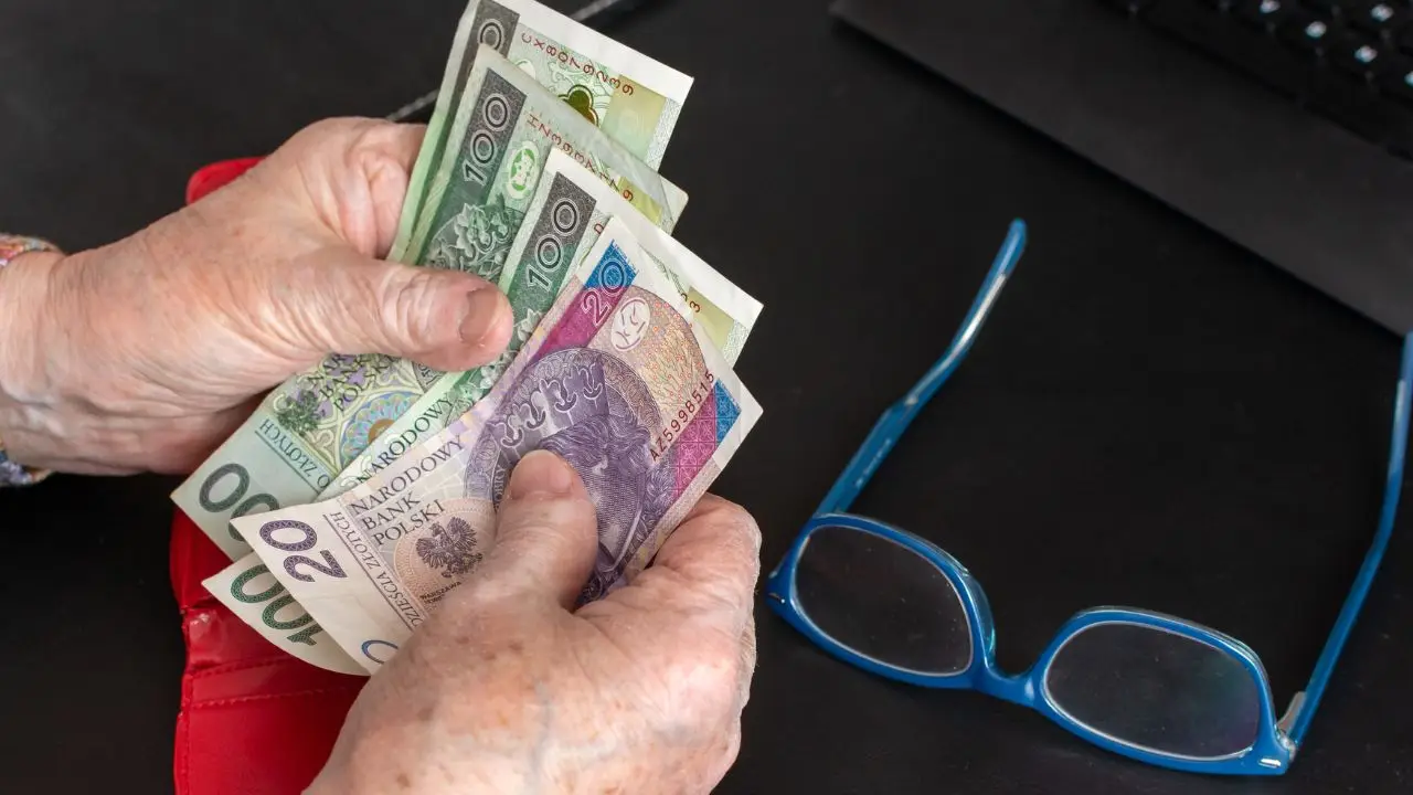 Wyrównania dla emerytów - pieniadze w dłoni emerytki, obok okulary