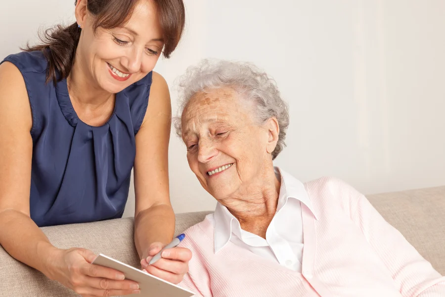 Opiekunka seniorów pokazuje notes seniorce i się uśmiechają.
