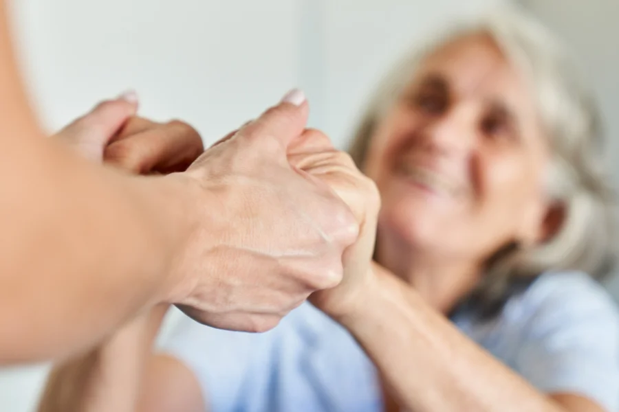 Wsparcie seniorki przez opiekunkę - trzymają się za dłonie.