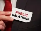 PR - napis public relations na plakietce trzymanej w dłoni przez osobę w garniturze