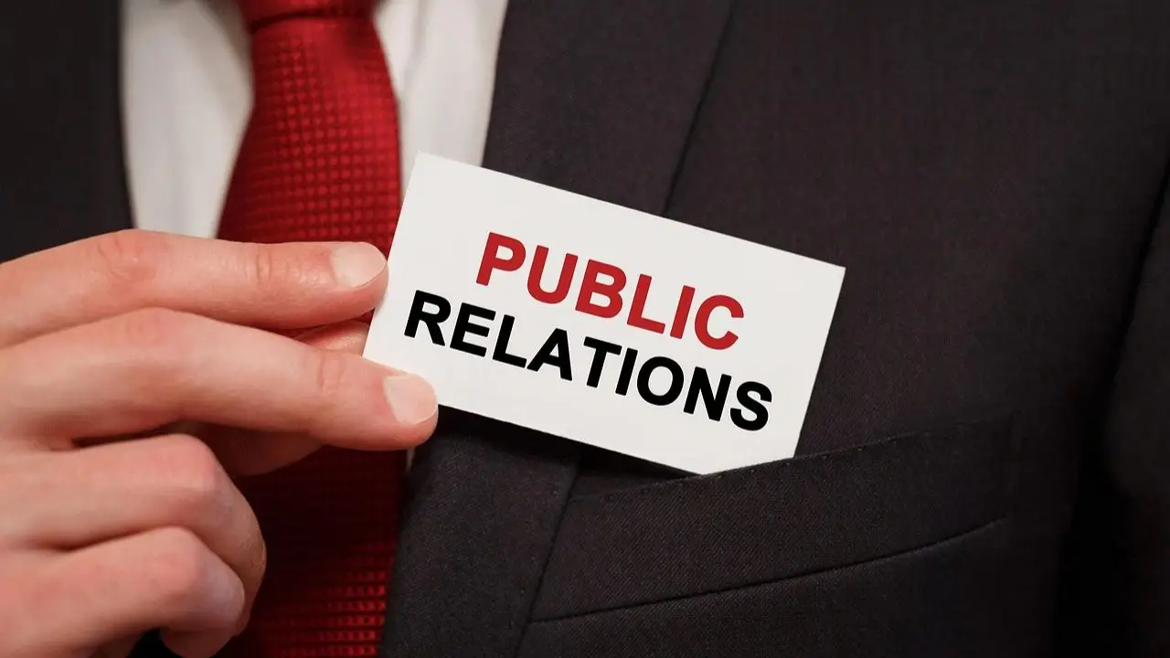 PR - napis public relations na plakietce trzymanej w dłoni przez osobę w garniturze